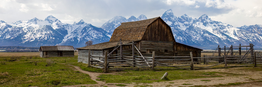 Rustic wooden John Moulton Barn with Grand Teton Mountains in the background under a cloudy sky.